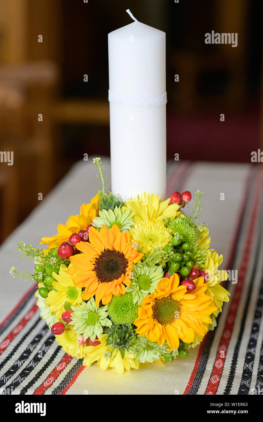 Baptismal candle with a sunflower bouquet in an Orthodox church in preparation for the baptism, first of seven Sacraments in the Orthodox Church Stock Photo