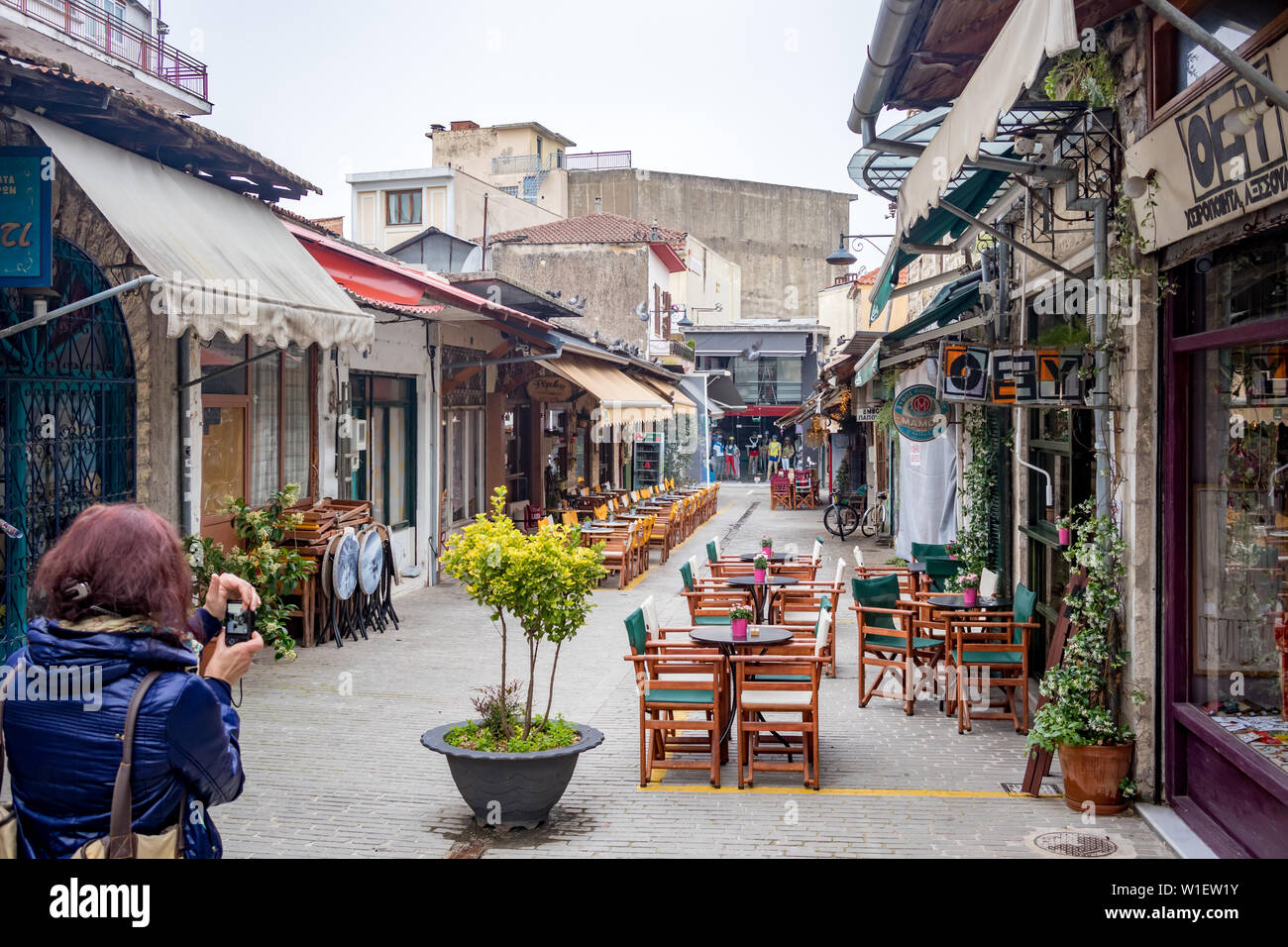 IOANNINA, GREECE - JUNE 6, 2019 - Female photographer with blue jacket takes photos of the empty cafeterias inside the center of the small beautiful old town Stock Photo