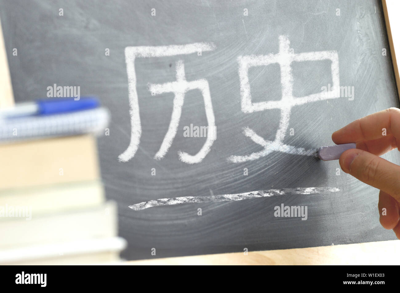 Hand writing on a blackboard in Chinese History class with the word History written on. Some books and school materials. Stock Photo