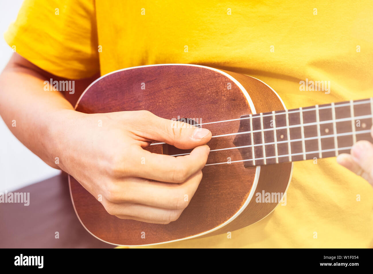 Young playing wooden ukulele shiny Stock Photo