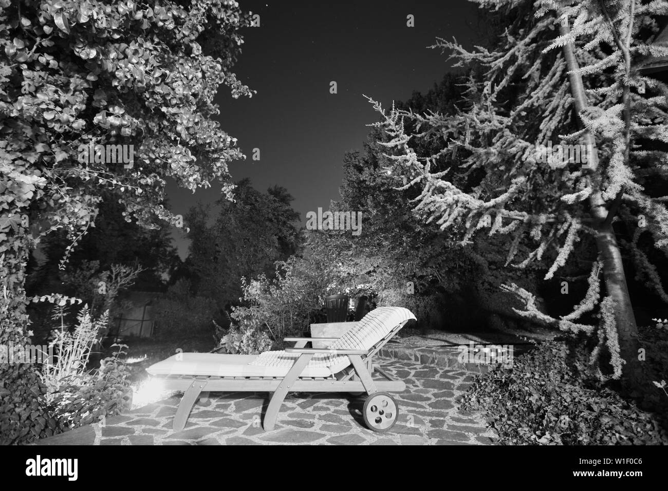 Wooden chaise longue in the picturesque corner of the garden at night. Croatia. Stock Photo