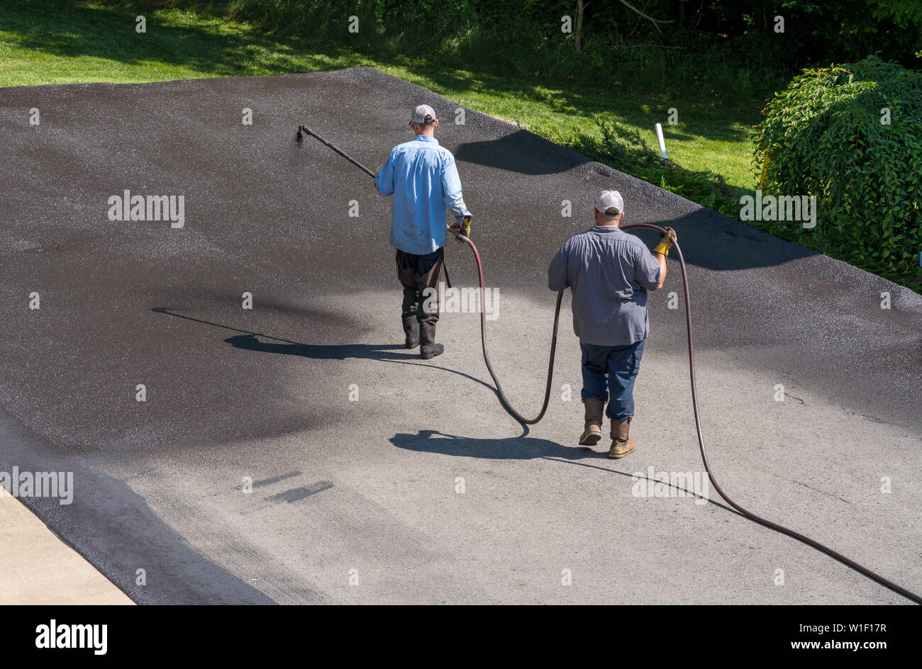 Workers spraying blacktop or asphalt sealer onto roadway Stock Photo