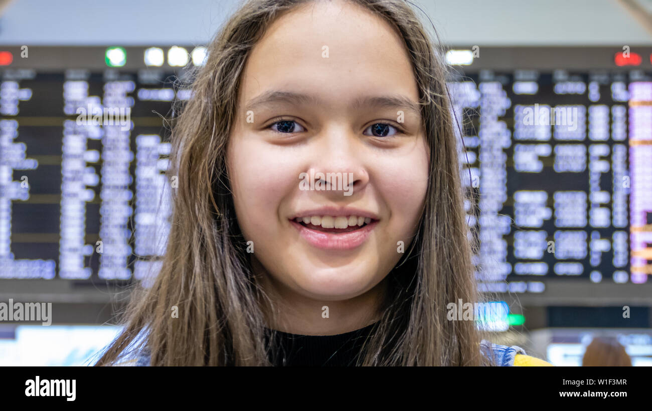 Asian American tween girl in front of airport arrivals board Stock Photo