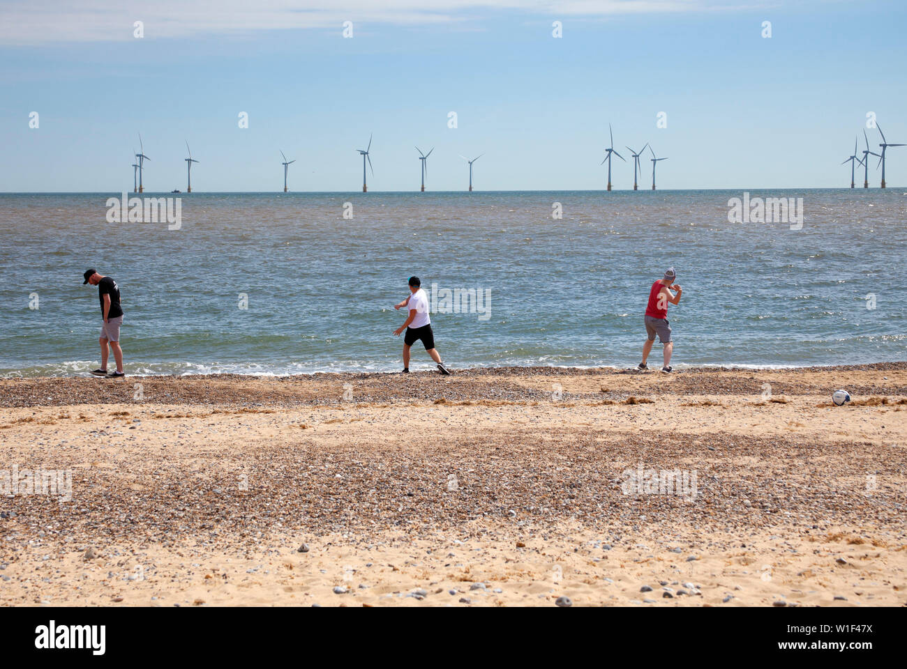 Thee men stone skimming in front of Scroby Sands windfarm, Great Yarmouth, England, UK Stock Photo