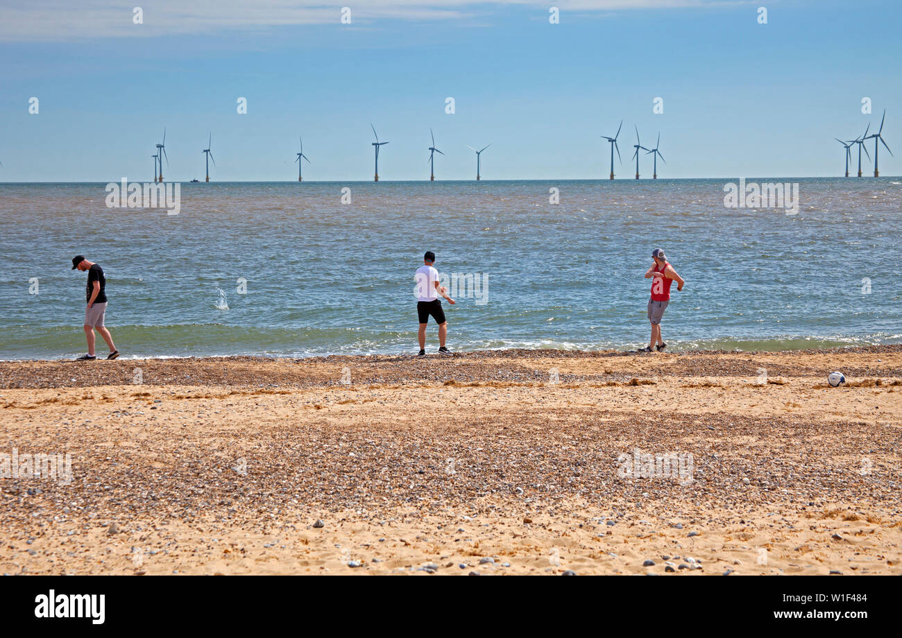 Thee men stone skimming in front of Scroby Sands windfarm, Great Yarmouth, England, UK Stock Photo