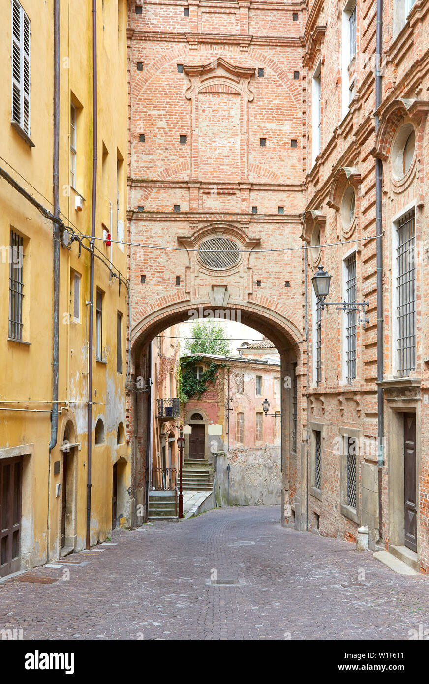 Ancient, empty street with red bricks building and arch in a summer day in Mondovi, Italy Stock Photo