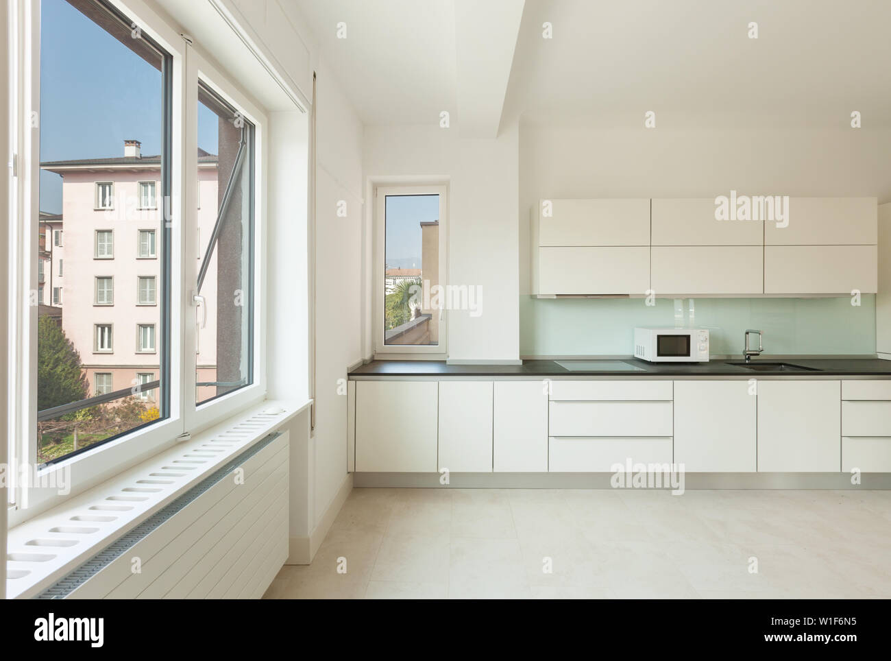 A modern kitchen with charcoal custom cabinets, a marble back splash tile,  and kitchen sink with a chrome faucet in front of a large window Stock  Photo - Alamy