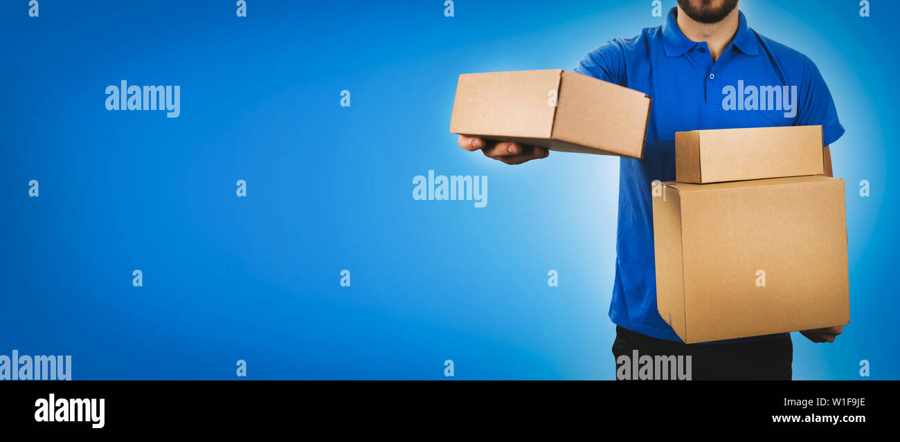 delivery service man holding cardboard boxes on blue background copy space Stock Photo