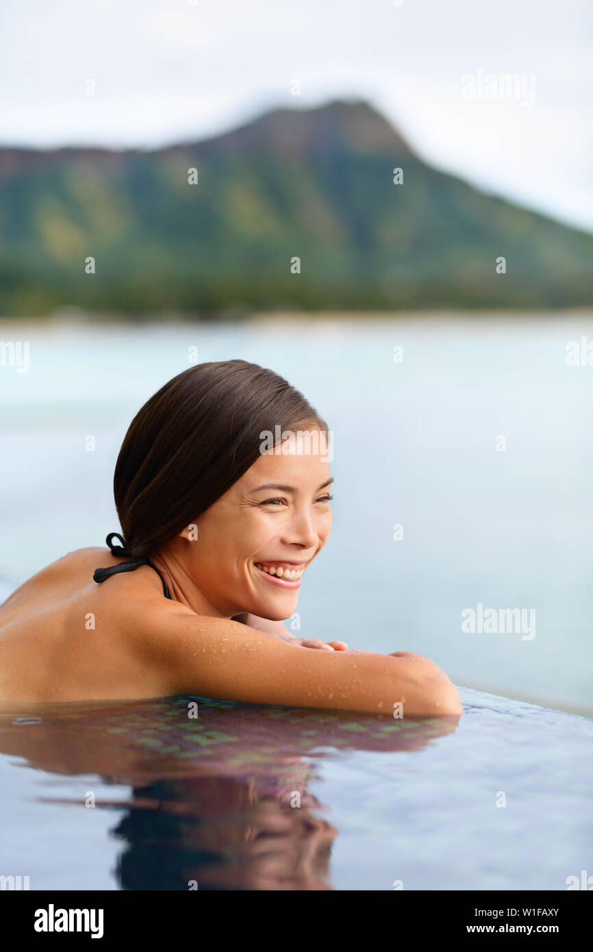 Holiday woman swimming at beach on Hawaii travel. Asian chinese young lady relaxing in infinity pool in luxury hotel resort on Waikiki beach in Honolulu, Oahu, Hawaii, USA. Stock Photo