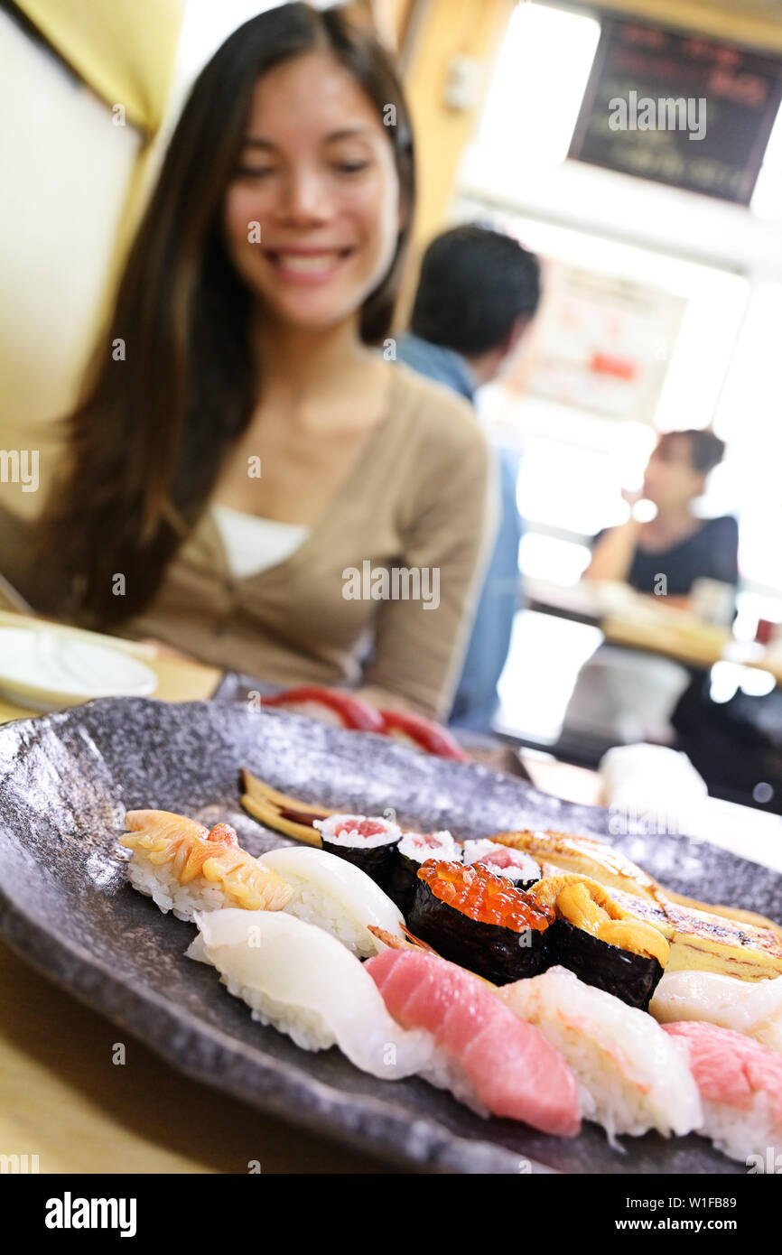 Sushi eating woman tourist in Tokyo restaurant. Travel destination famous Tsukiji Fish Market, person looking at plate of raw seafood presented as sashimi. Japanese food. Stock Photo