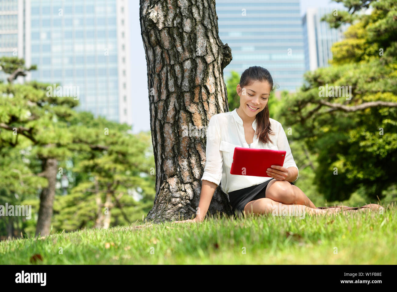 Asian business woman reading using tablet app in Tokyo. Young adult student studying e book with pc touchpad ereader computer or digital tablet in park near Ginza district, downtown of Tokyo, Japan. Stock Photo