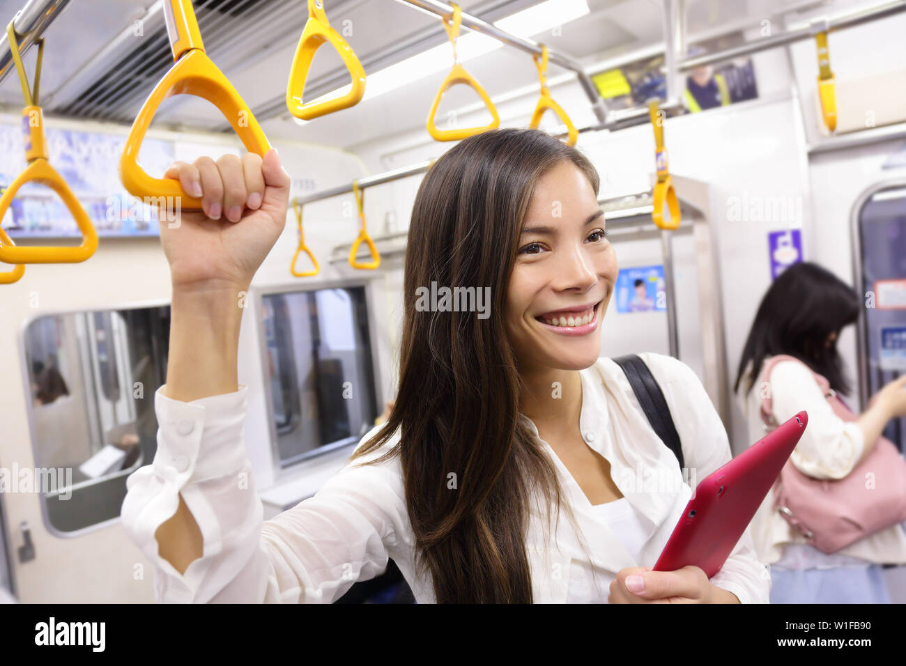 Subway commuter woman on Japanese public transport in Tokyo, Japan. Tourist using Japan's capital city metro system to commute. Portrait of happy asian lady holding handhold inside the wagon. Stock Photo