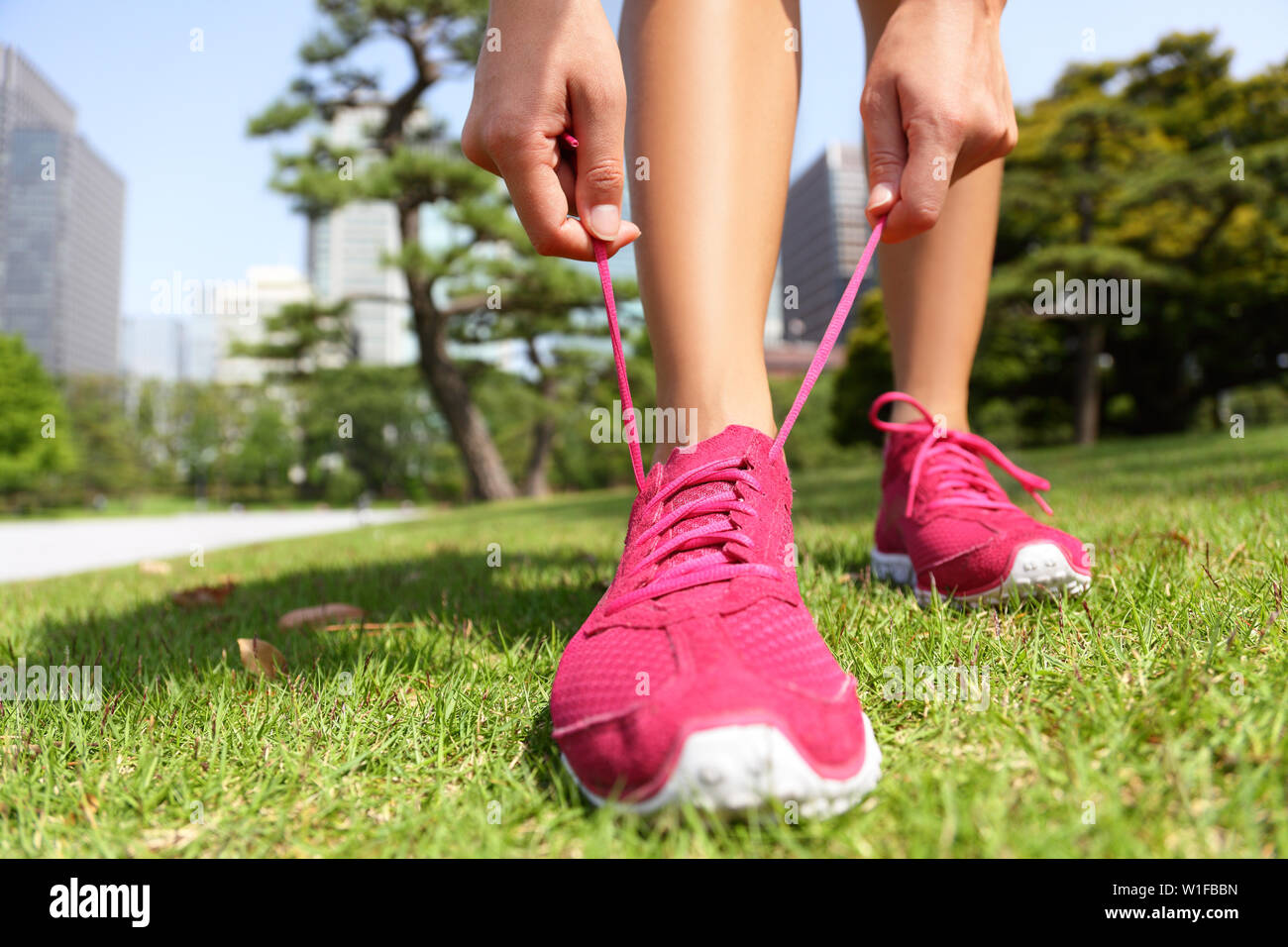 Runner getting ready for jogging tying running shoes laces - Woman preparing before run putting on trainers in japanese park near Ginza in Tokyo, Japan Stock Photo