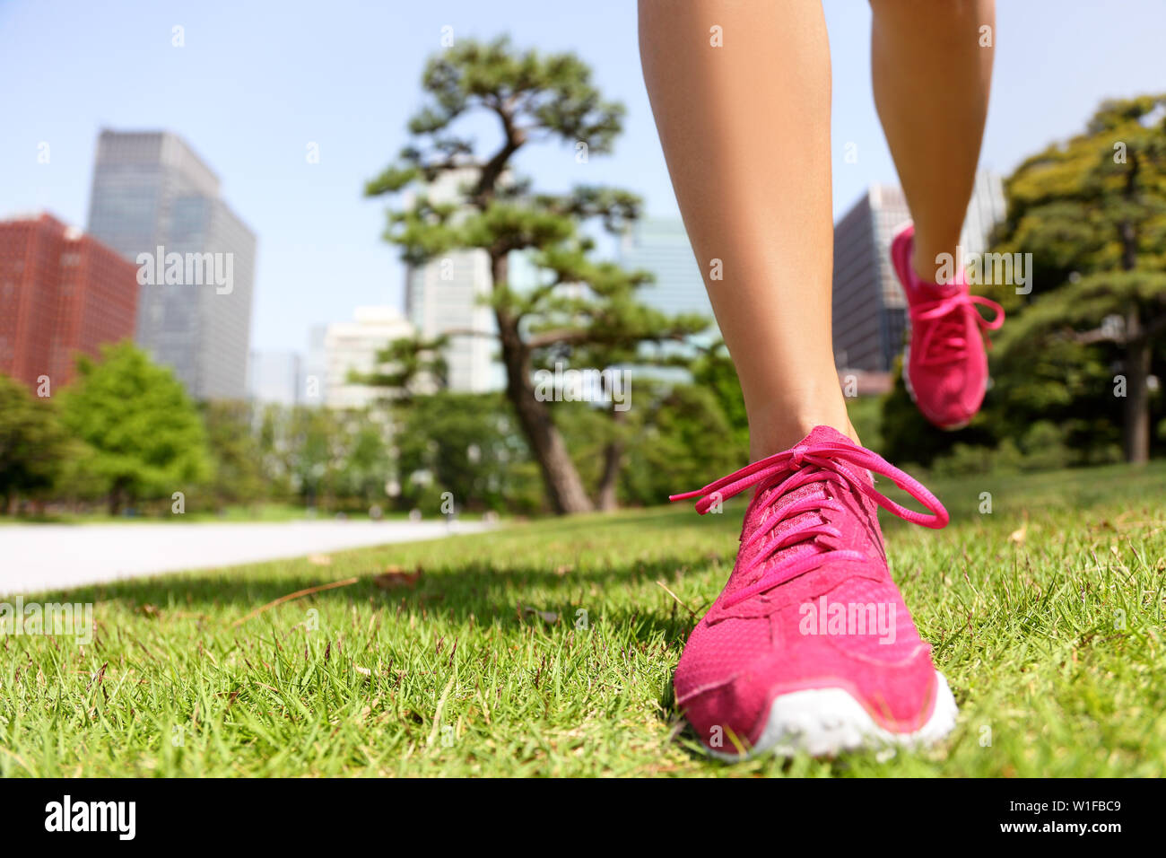 Running shoes - woman runner jogging staying fit in Tokyo Park, Japan. Closeup of pink trainers in green grass in summer park near the Imperial Palace and Ginza district downtown. Stock Photo