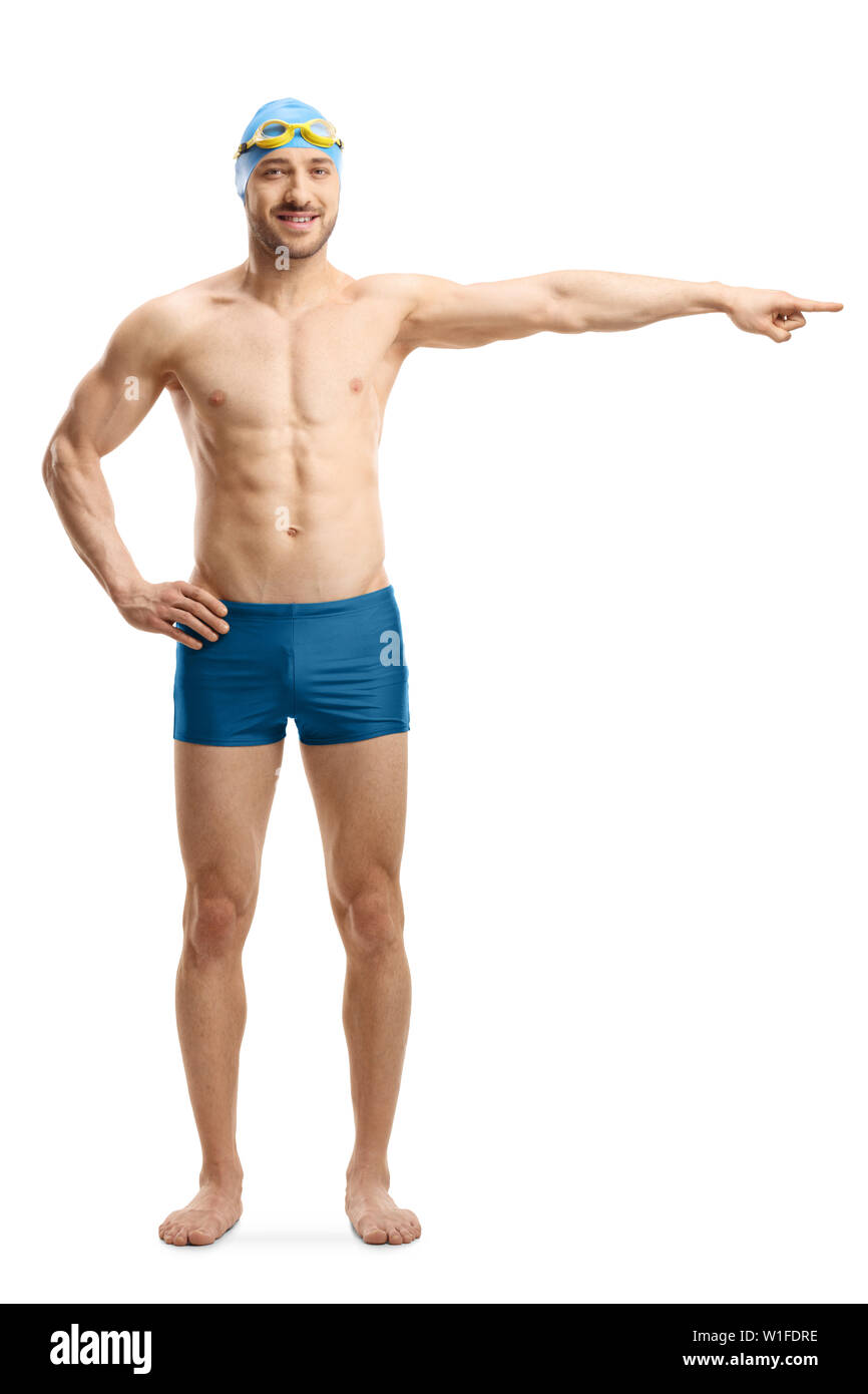 Full length portrait of a young man in swimming shorts, googles and a cap pointing to the side isolated on white background Stock Photo