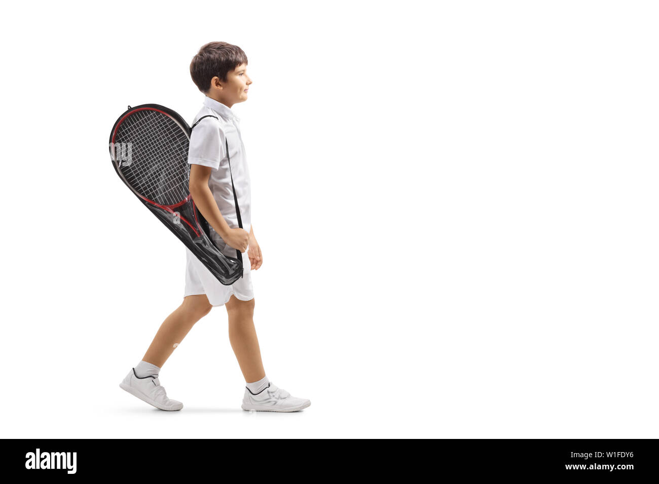 Full length profile shot of a boy walking with a tennis racket in a case isolated on white background Stock Photo