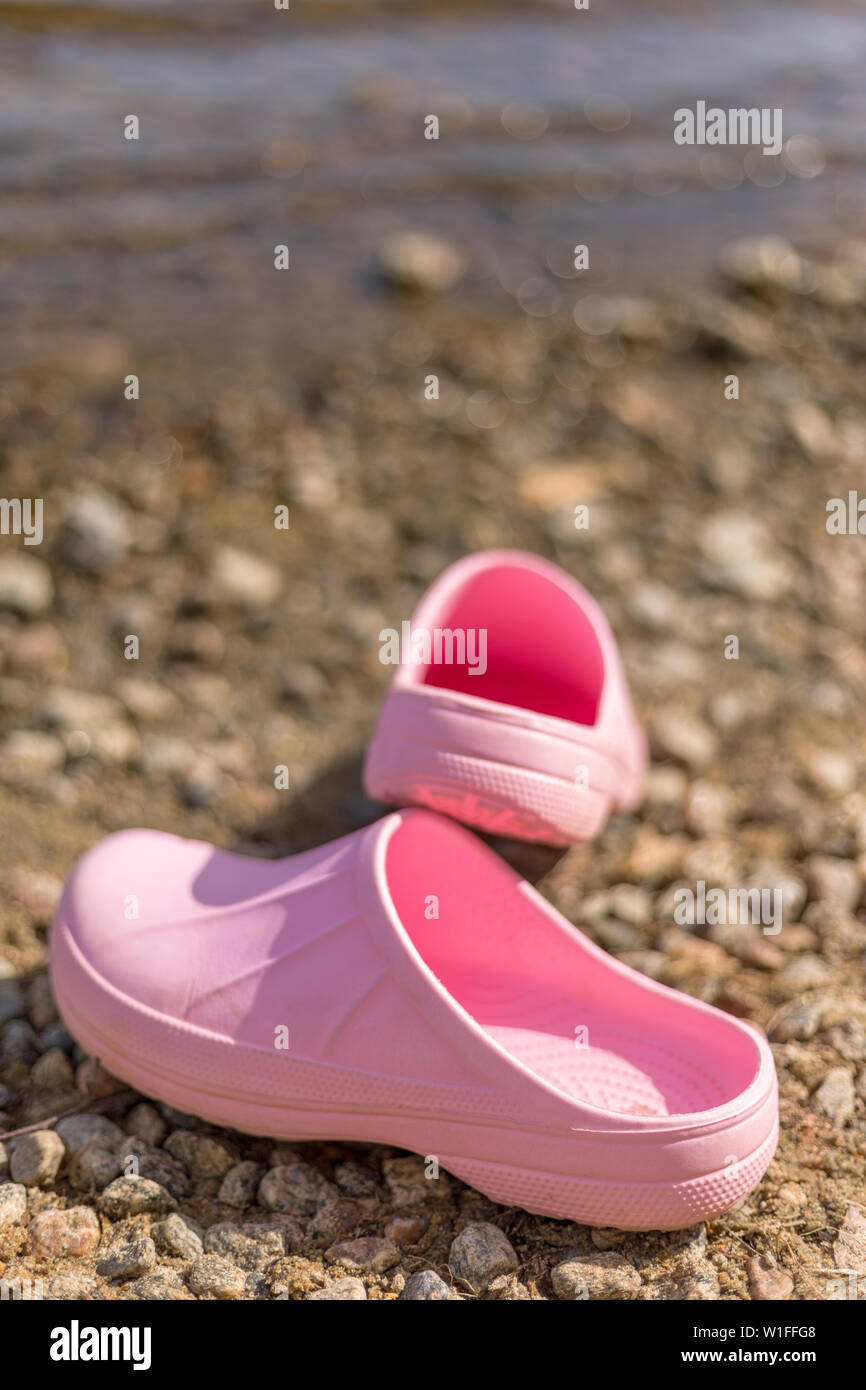 Pair of pink plastic clogs on shoreline beach in the summer Stock Photo