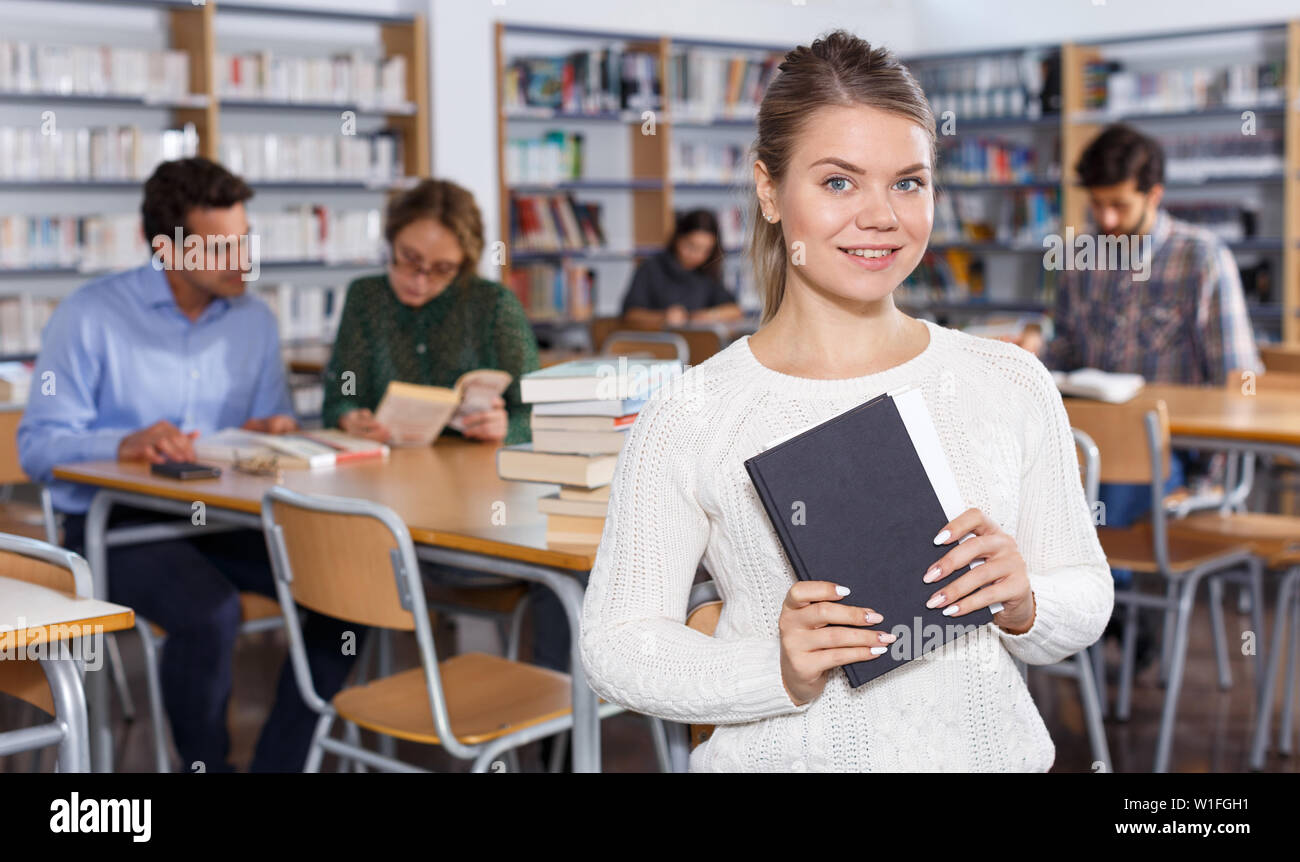 Portrait of happy modern girl with books in hands sitting in classroom ...