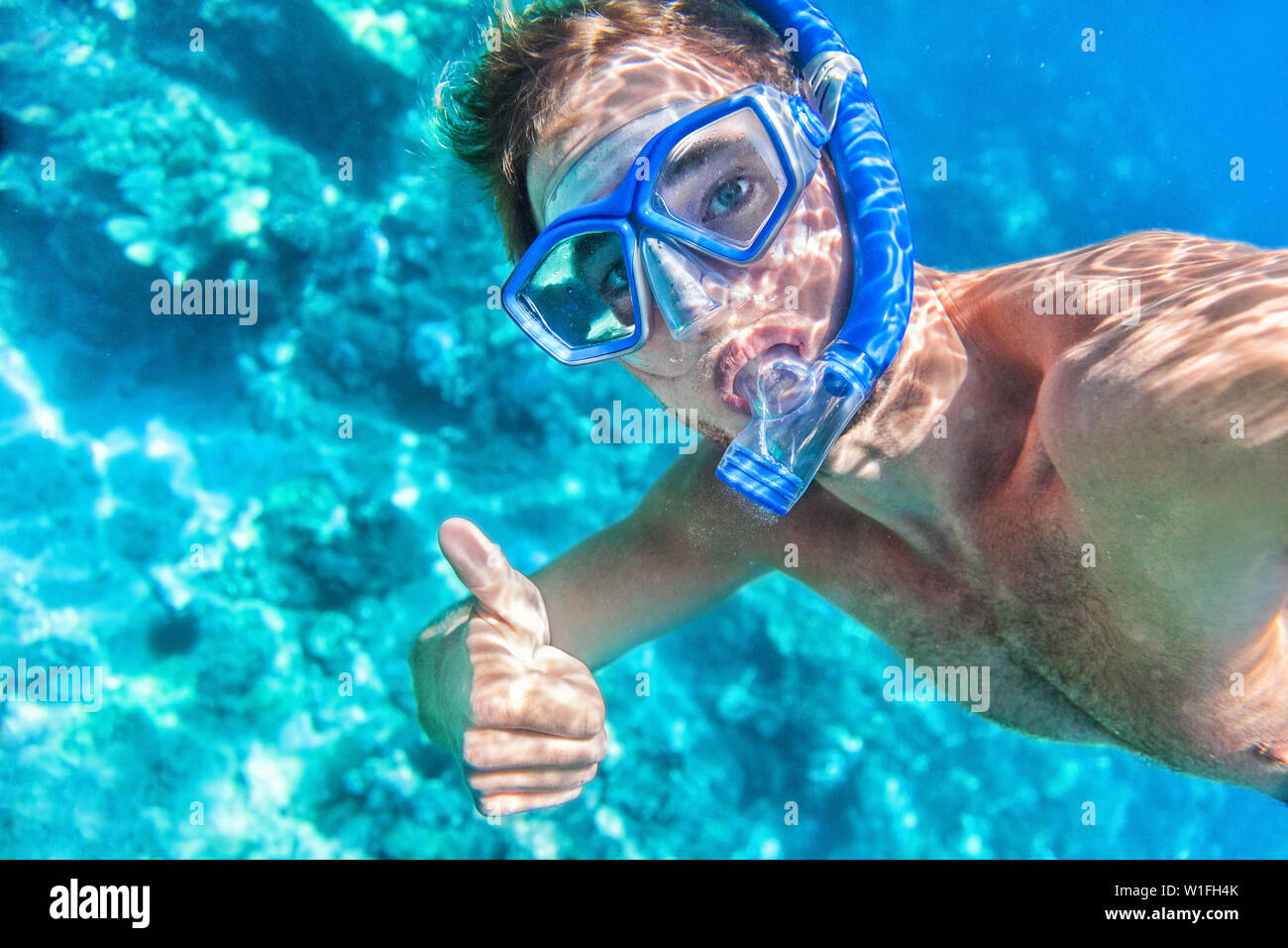 Snorkeling man underwater giving thumbs up ok signal wearing snorkel and mask having fun on beach summer holidays vacation enjoying recreational leisure time swimming in the sea. Stock Photo