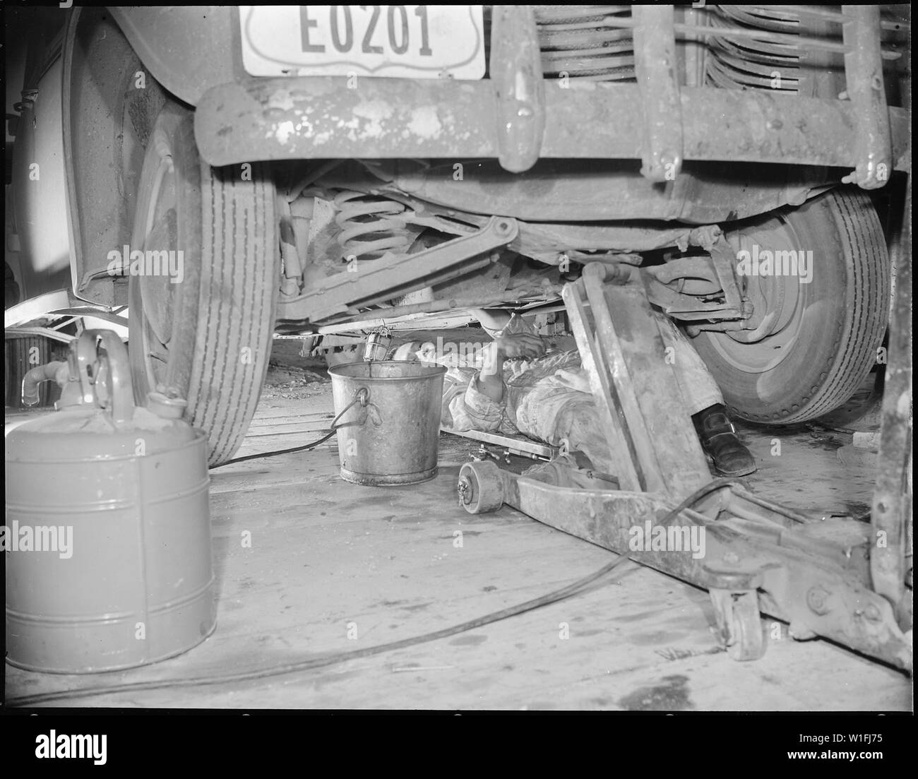 Jerome Relocation Center, Denson, Arkansas. A young Nisei mechanic under a project car in a tempora . . .; Scope and content:  The full caption for this photograph reads: Jerome Relocation Center, Denson, Arkansas. A young Nisei mechanic under a project car in a temporary shop. Stock Photo