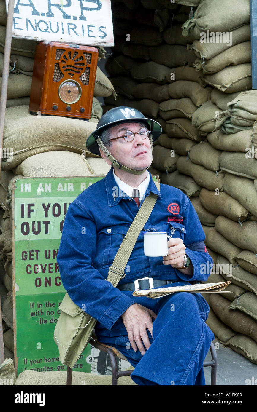 Kidderminster, UK. 29th June, 2019. Severn Valley Railways 'Step back to the 1940's' gets off to a fabulous start this weekend with costumed re-enactors playing their part in providing an authentic recreation of wartime Britain. An ARP (air raid precaution) warden sits on duty outside an air raid shelter, having a cuppa, at a vintage railway station along the heritage railway line. Credit: Lee Hudson Stock Photo