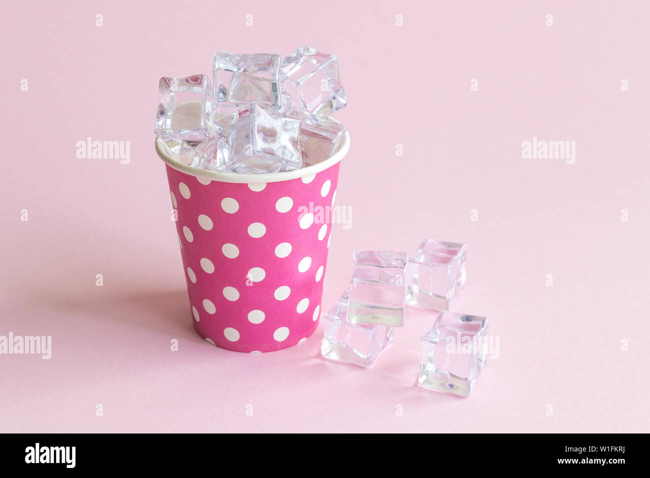 Paper cup polka design full of ice cubes against pastel pink background ...
