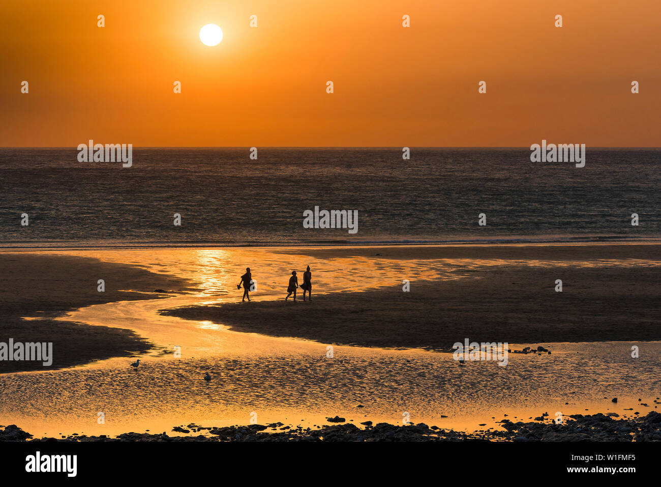 People seen in silhouette as a beautiful sunset sets over Fistral Beach in Newquay in Cornwall. Stock Photo