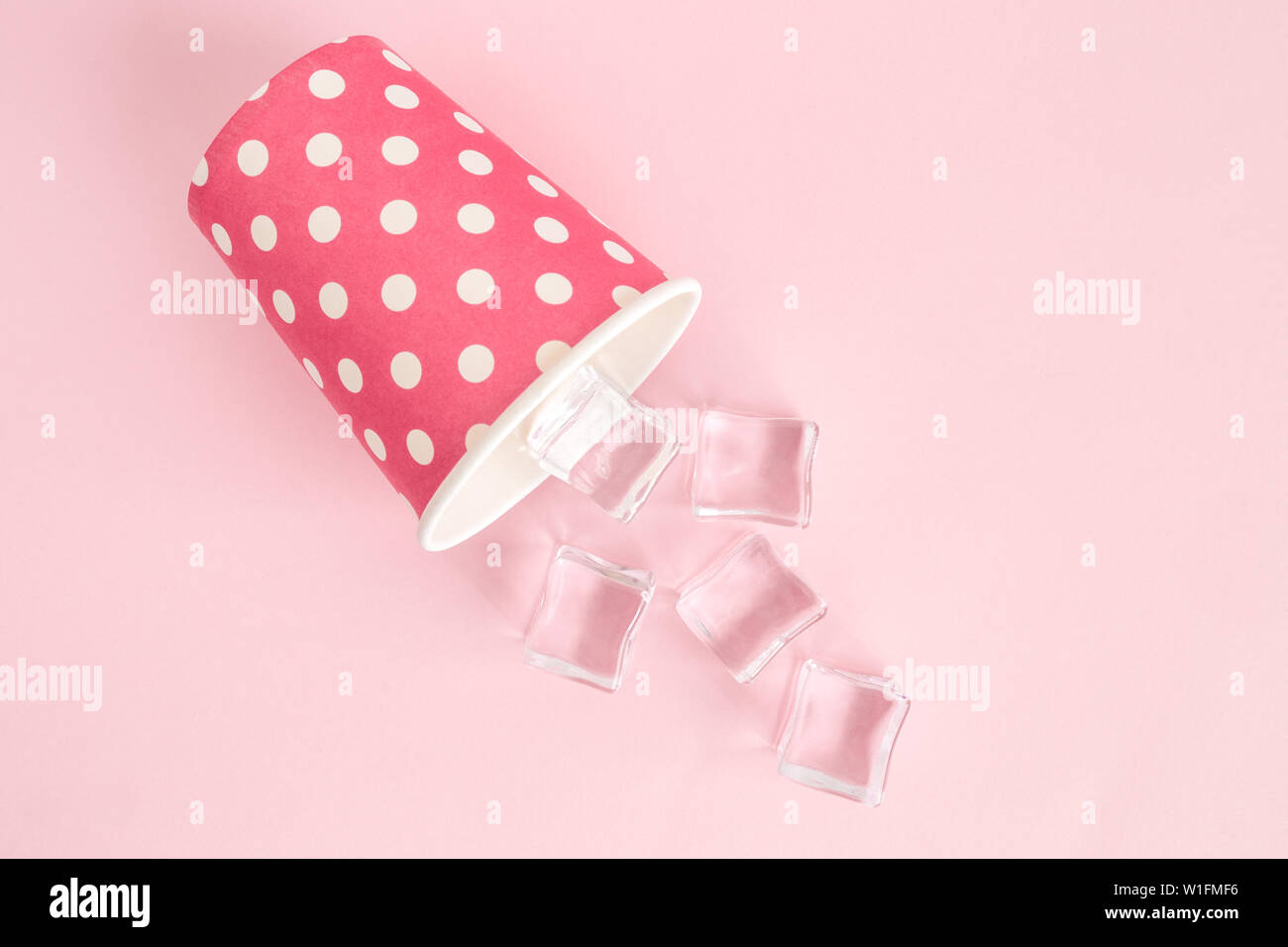 Flat lay of paper cup polka design with ice cubes against pastel pink ...