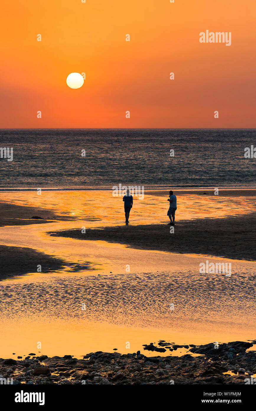 People seen in silhouette as a beautiful sunset sets over Fistral Beach in Newquay in Cornwall. Stock Photo