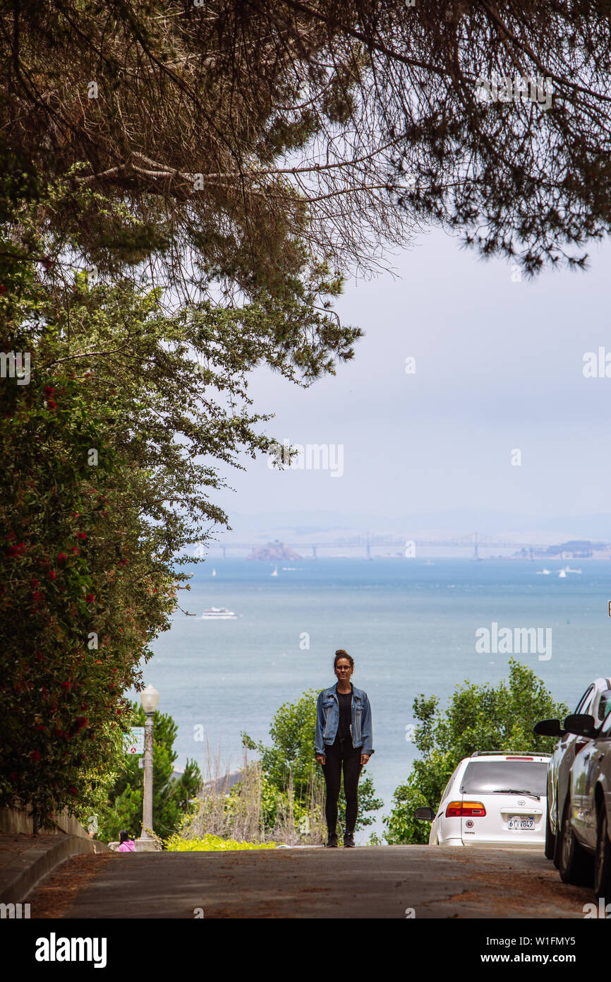 Woman standing in the middle of the street in San Francisco with the Bay Bridge on the back, California, USA Stock Photo