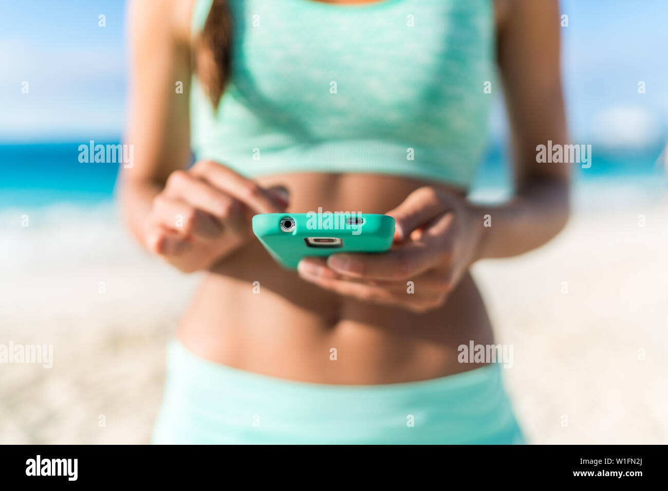 Athlete using mobile phone app fitness tracker for tracking weight loss progress during running exercise. Fit girl woman touching smartphone texting or playing online games or video workouts. Stock Photo