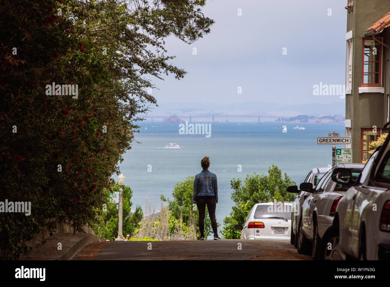 Woman taken from behind standing in the middle of the street in San Francisco facing the Bay Bridge on the back, California, USA Stock Photo