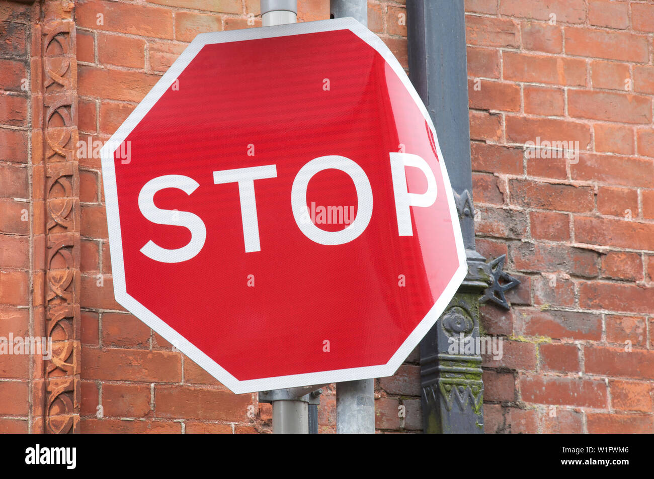 STOP! Oops too late. An octagonal red stop sign at a narrow and restricted street junction. Traffic sign bent out of shape by a collision. England, UK. Stock Photo