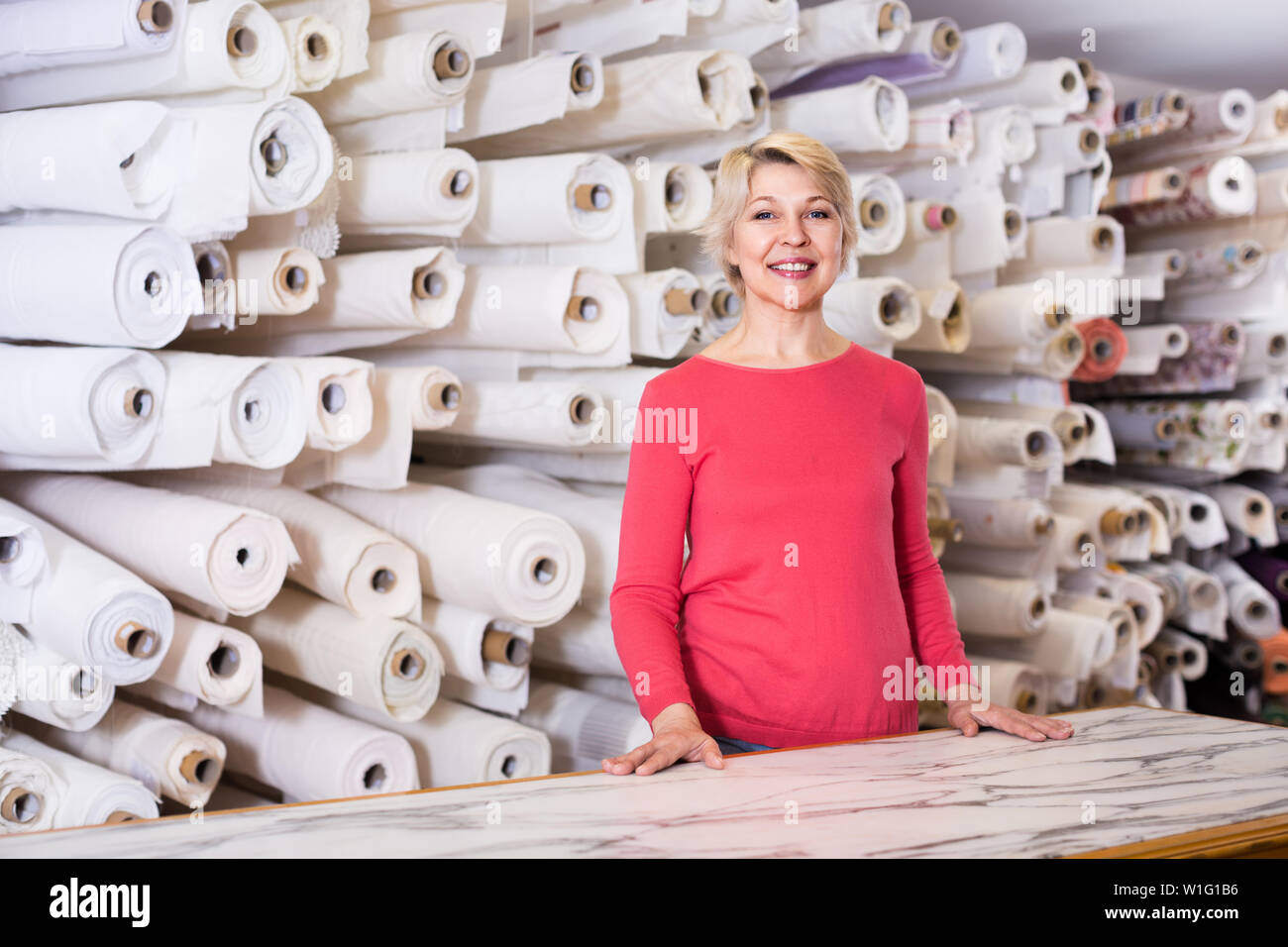 Mature woman buyer is showing bought home textiles in textile shop