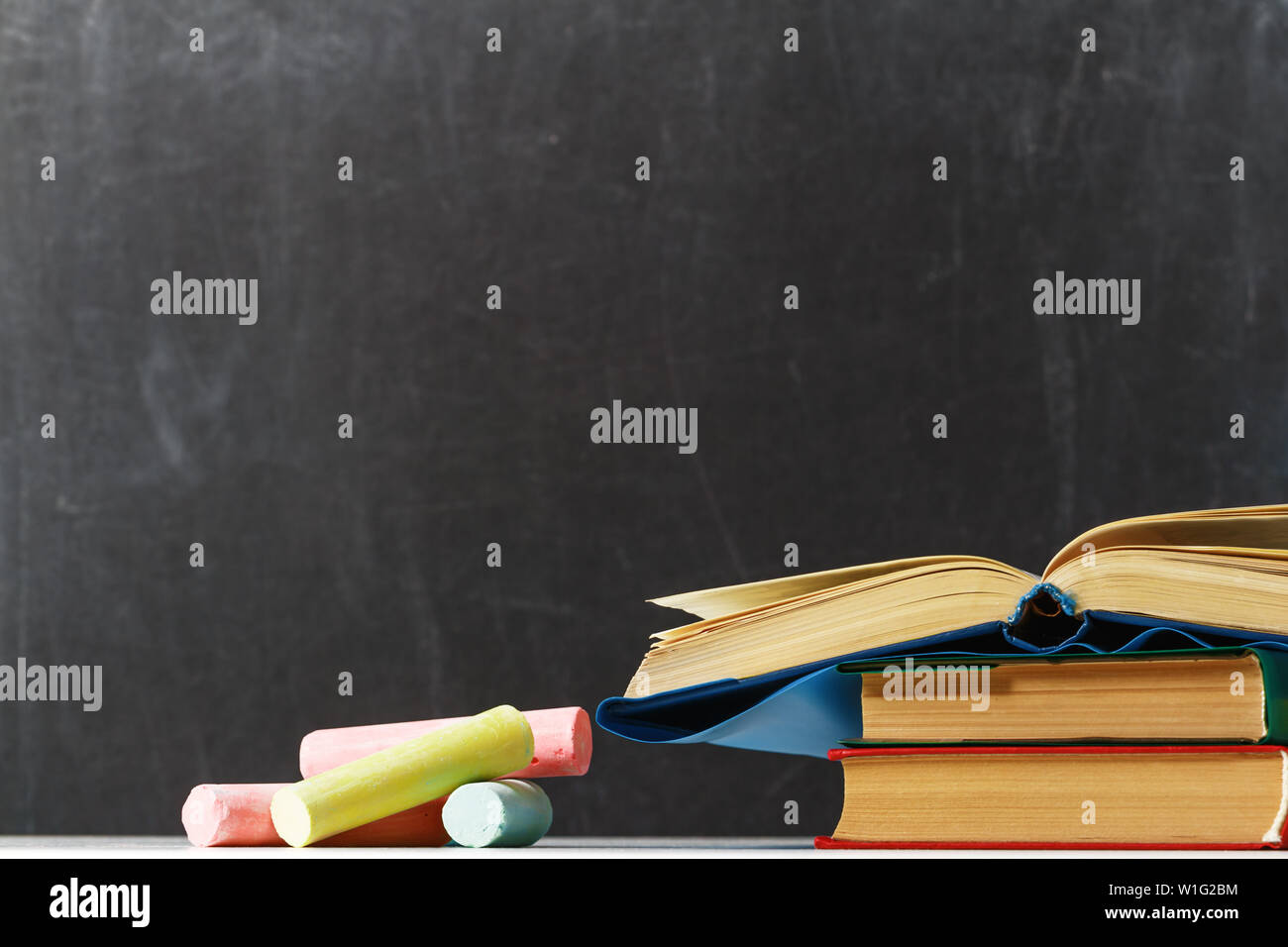 A stack of books and multi-colored chalk on the background of the blackboard school. The concept of education. Back to school. Copy space. Stock Photo