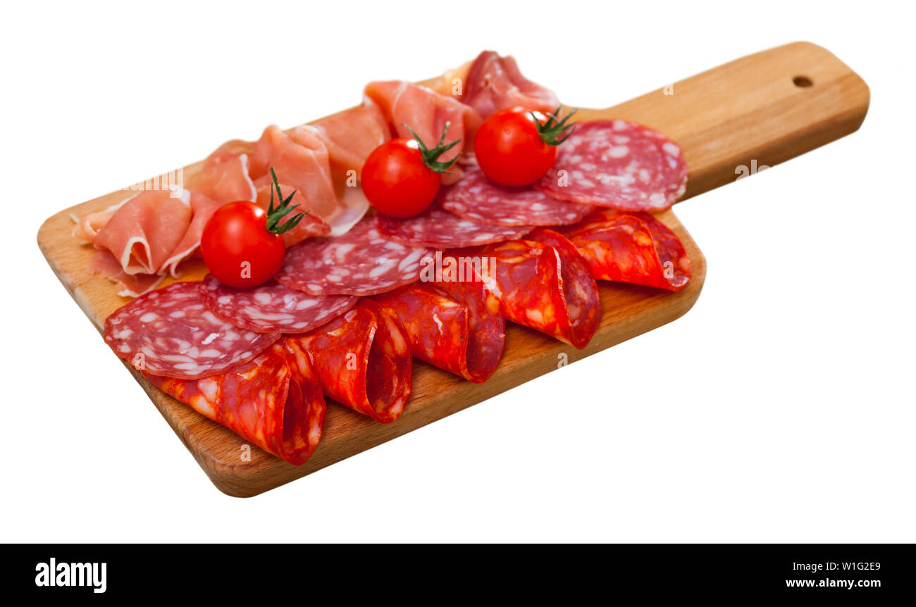 Appetizing cold cuts from Spanish ham and spicy dry-cured sausages with cherry tomatoes on wooden board. Isolated over white background Stock Photo