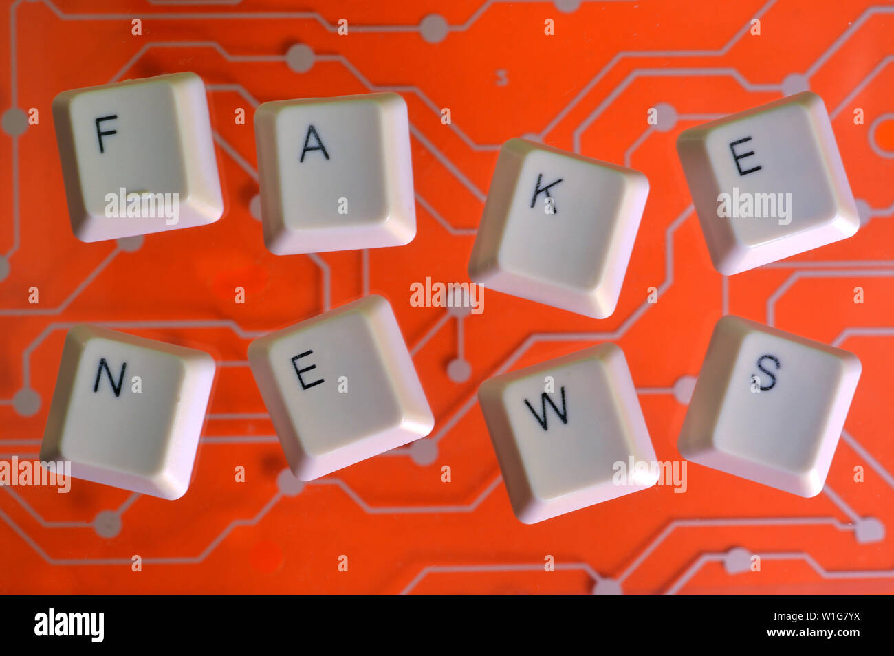 Keyboard keys form the word FAKE NEWS on orange electric circuit in the