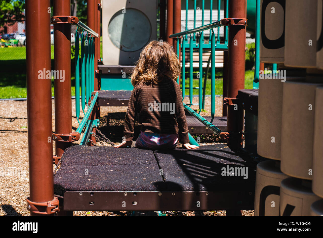 A young girl sits on playground equipment on a warm summer day. Stock Photo