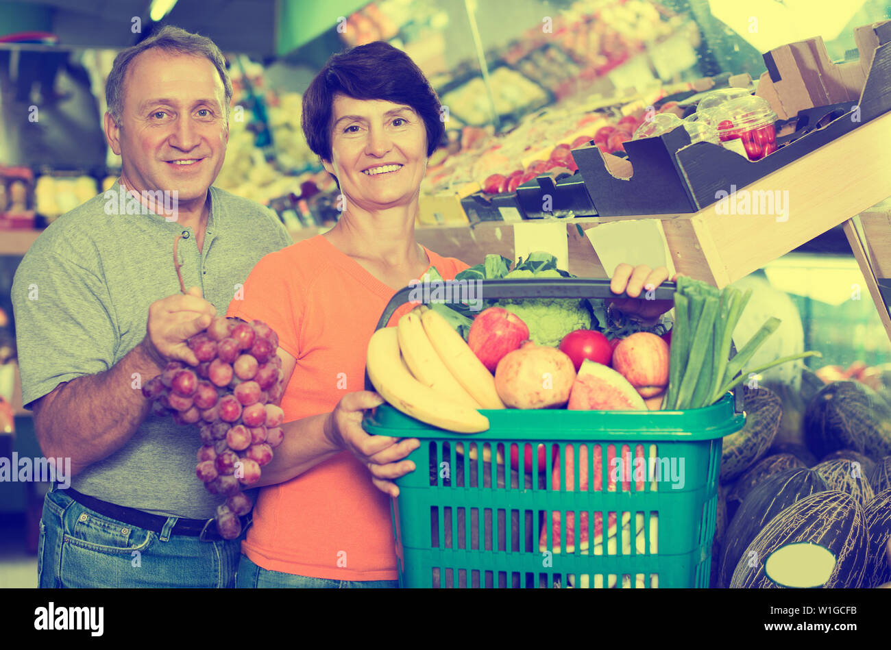 elderly male with female are standing with basket of purchases in the