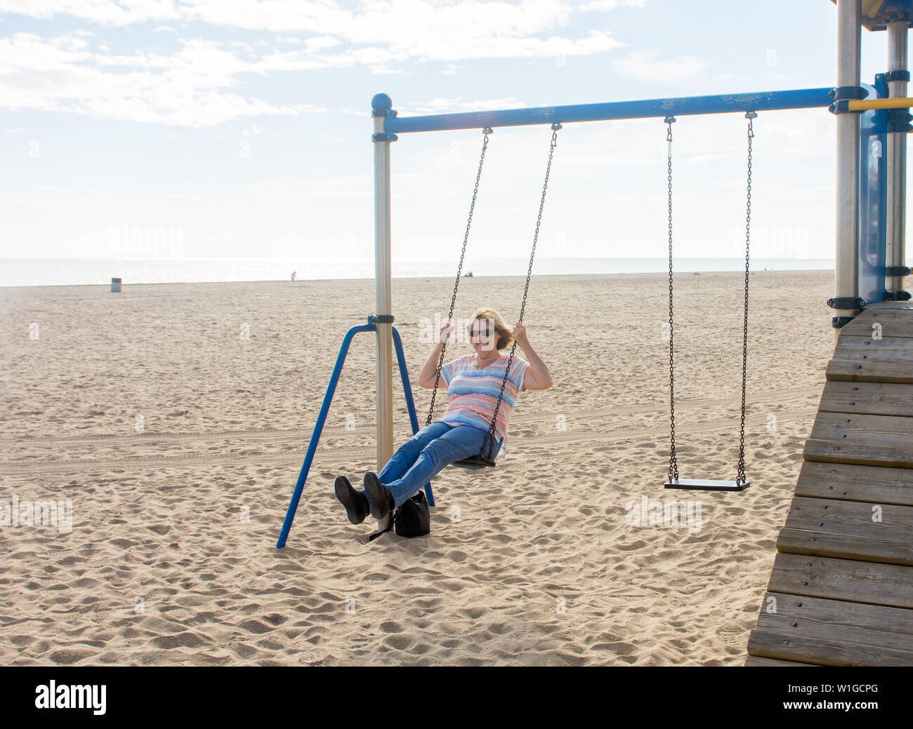 Senior woman enjoying retirement life feeling happy and healthy having fun swinging on a swing in the beach in a sunny beautiful day. In Active old pe Stock Photo