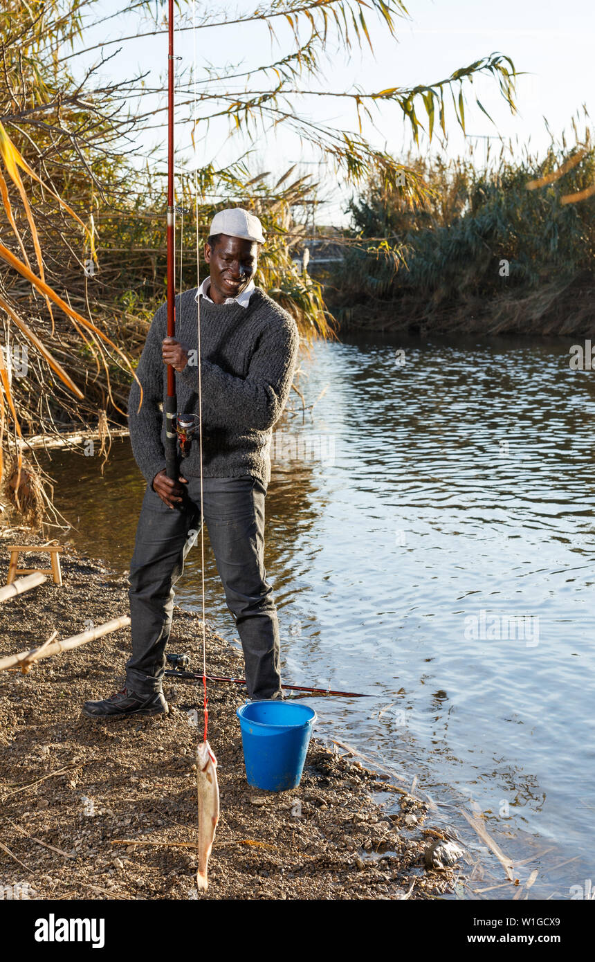 Mature African man standing near river and pulling fish on hook Stock Photo