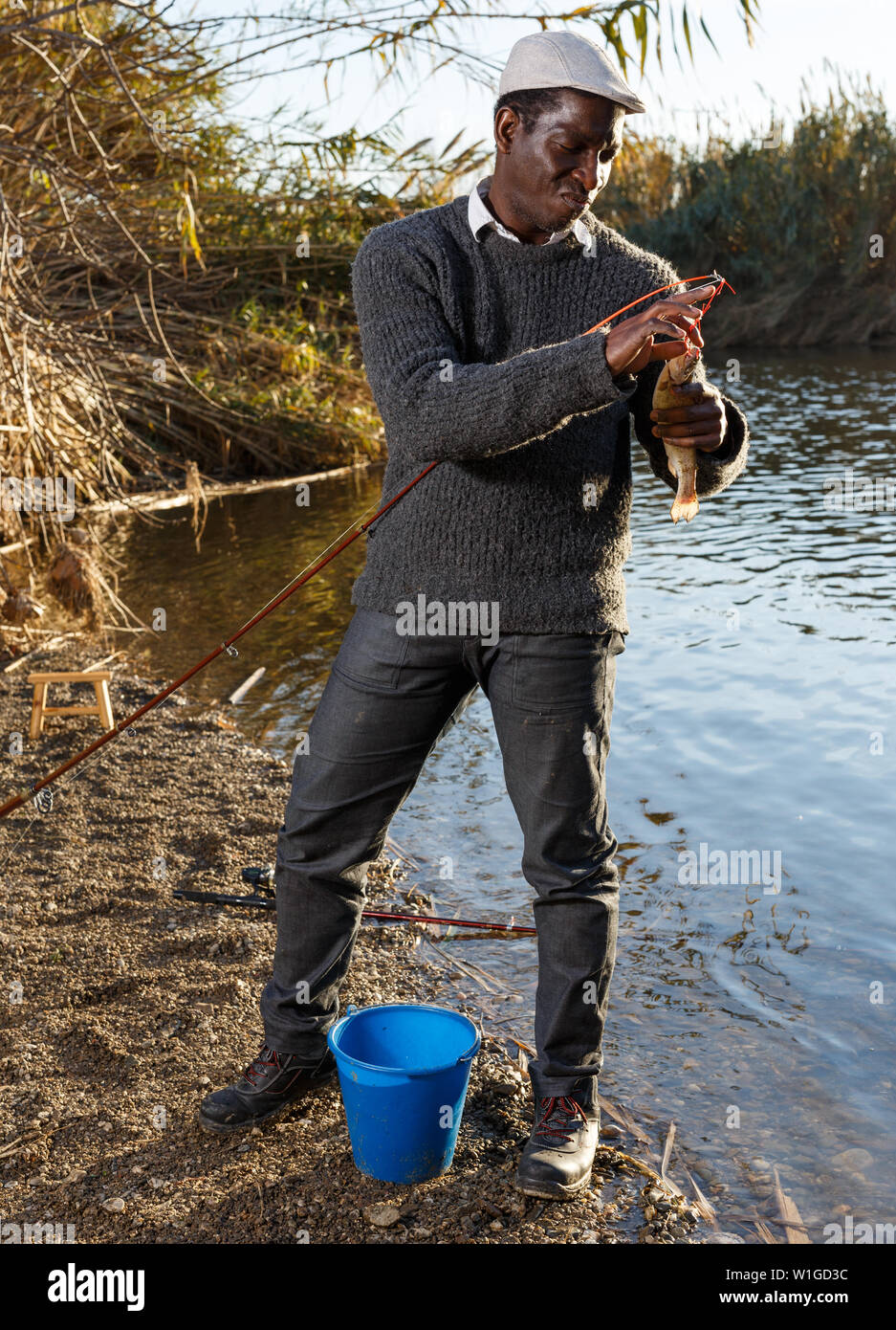Mature African man standing near river and pulling fish on hook Stock Photo