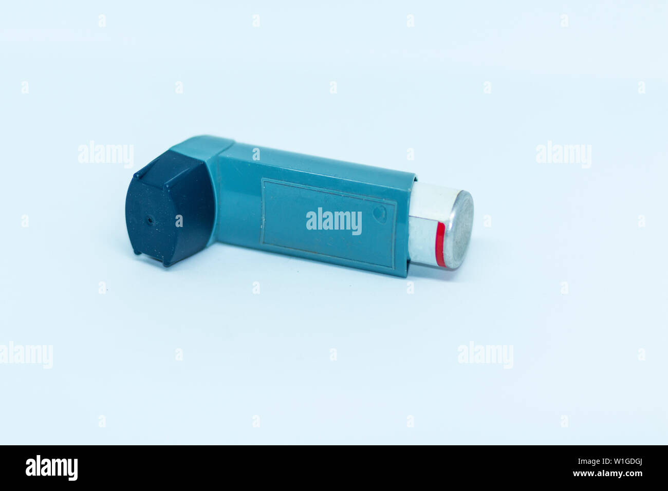 One blue asthma inhaler is laying on its side in front of a what backgrond. Stock Photo