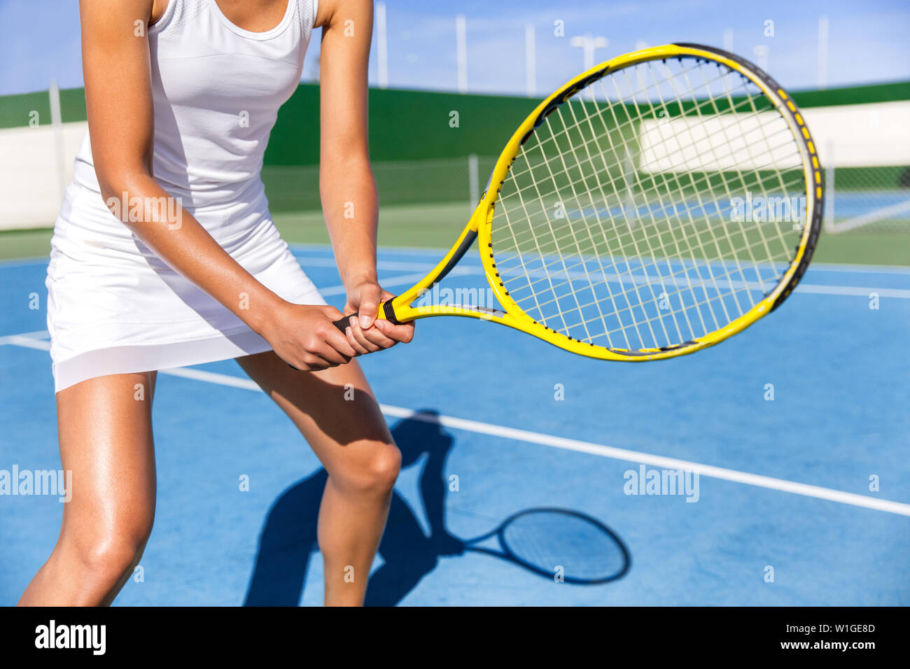 Midsection of tennis player woman ready playing game on blue hard court outdoor in position holding racket wearing white dress skirt. Female athlete sporty girl for summer sports activity course. Stock Photo