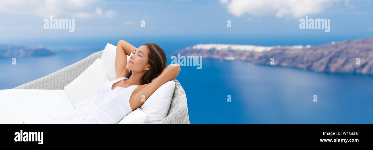 Relaxing woman sleeping on outdoor daybed patio furniture enjoying view of Mediterranean sea Europe travel destination. Asian girl lying down on pillows dreaming carefree happy. Luxury home living. Stock Photo