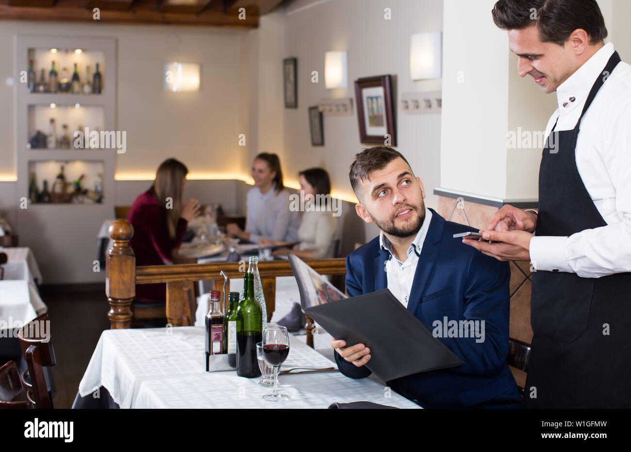 Hospitable waiter taking order in cafe, helping young male with menu