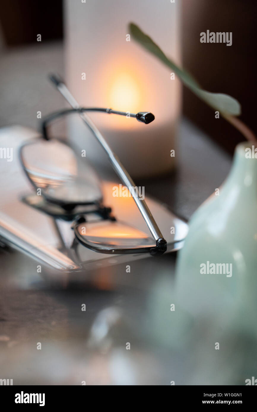 eye glasses folded up on a tables reflecting  the light of a candle Stock Photo