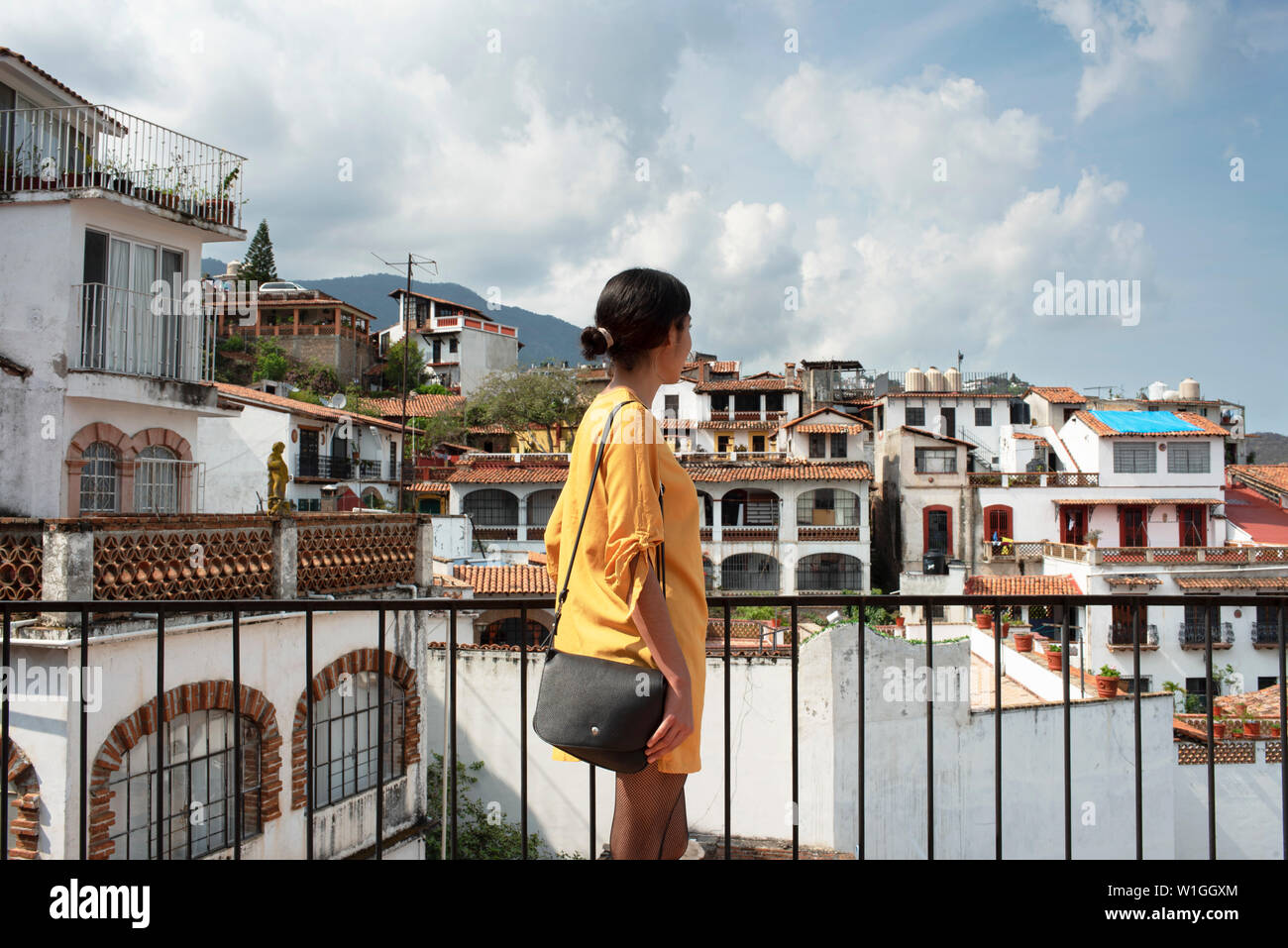 Rear view of latina girl overlooking the scenic town scape of white houses. Sightseeing in Taxco, Guerrero State, Mexico. Jun 2019 Stock Photo