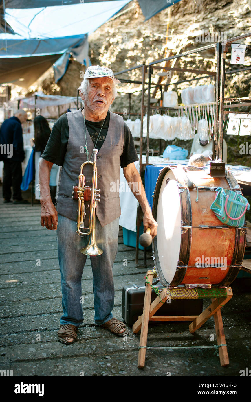 Elderly latino man singing and playing music with his trumpet and drum at Saturday's silver market. Taxco de Alarcón, Mexico. Jun 2019 Stock Photo