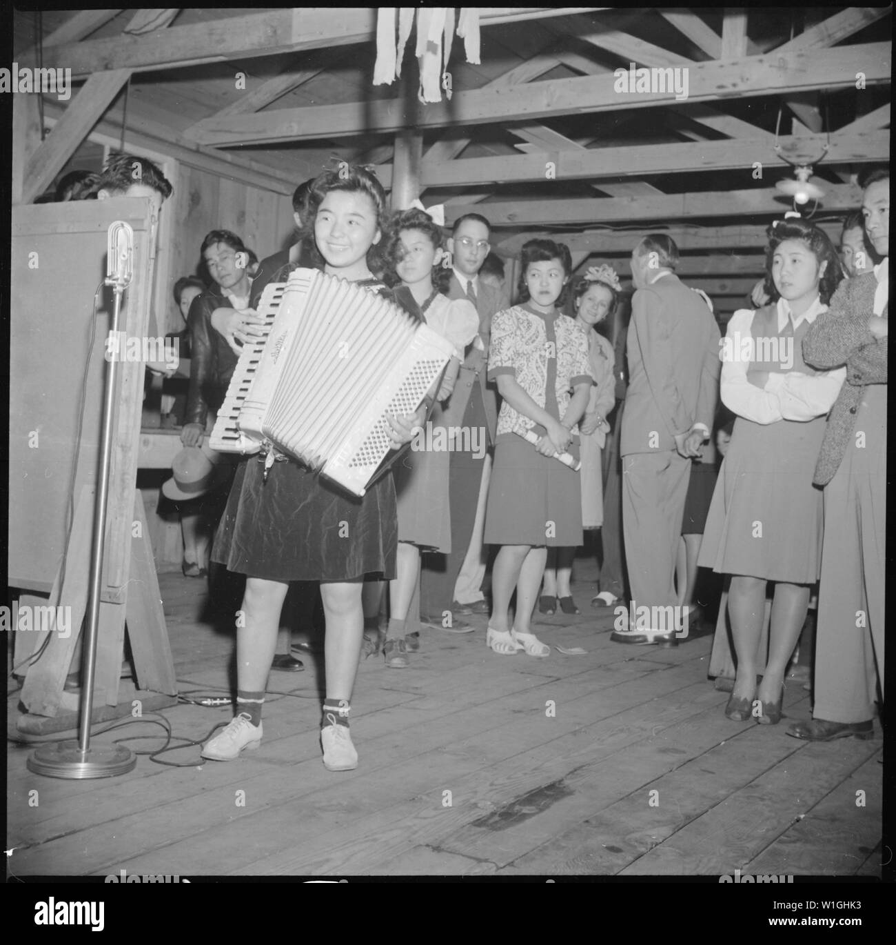 Manzanar Relocation Center, Manzanar, California. A young evacuee of Japanese ancestry entertains o . . .; Scope and content:  The full caption for this photograph reads: Manzanar Relocation Center, Manzanar, California. A young evacuee of Japanese ancestry entertains on an accordion at a dance given by the Girls' Relocation Committee for fellow evacuees. Stock Photo